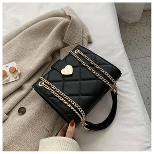 Close-up of black quilted shoulder bag with gold heart clasp and chain strap detailing