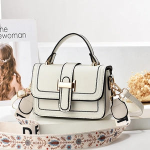 Weiße Ledertasche mit breitem Stickriemen und goldenen Metallteilen auf weißem Sockel