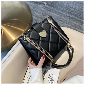 Detail of black quilted leather handbag with large gold heart-shaped rotating lock