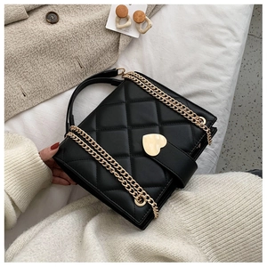 Close-up of black quilted leather tote with gold heart clasp on soft white fabric