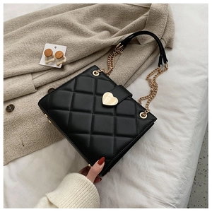 Close-up of black quilted leather shoulder bag featuring a gold heart-shaped buckle