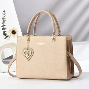 Beige structured leather tote bag with top handles and heart pearl charm in soft window light