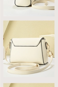 Detail view of cream crossbody bag with black piping and gold hardware on geometric stand