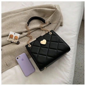 Detail of black quilted leather shoulder bag featuring a gold heart-shaped metal twist lock