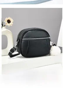 Detail view of black lychee grain crossbody bag with three zipper compartments and pompom