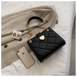 Close-up of black quilted leather tote with gold heart buckle and chain strap detail