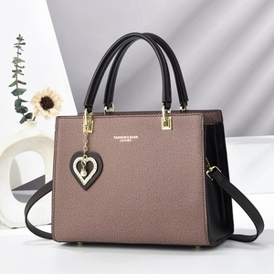 Brown textured tote bag with black handles and heart pearl charm in a minimalist setting