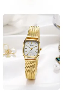 Close-up of golden square watch with mesh band on silk background with pearls