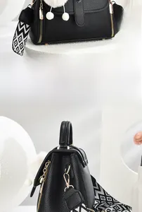 Détail du sac à main noir grainé avec bandoulière géométrique et pompon décoratif
