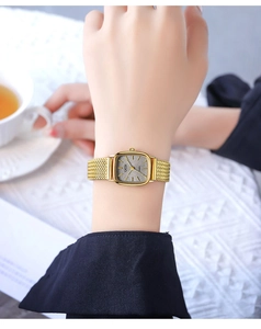 Detail of square gold quartz watch with grey textured dial and mesh band on wrist