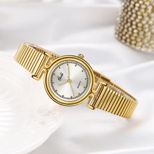 Elegante goldene Quarzuhr für Damen mit Stretcharmband auf weißer Seide und Keramikteller