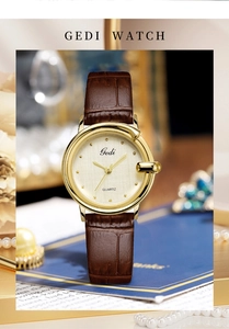 Elegant gold quartz watch with brown leather strap displayed with pearls on blue stand