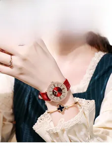 Détail d'une montre en cuir rouge avec lunette sertie et bracelet trèfle au poignet