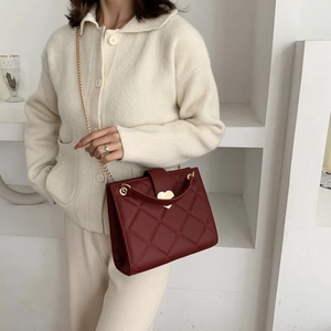 Elegant red quilted tote bag with gold heart lock shown on model with beige sweater