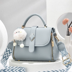 Nebelblaue Handtasche aus Leder mit geometrischem Gurt und dekorativem Plüschball