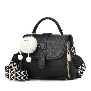 Black pebble leather handbag with geometric strap and plush pendant on white background