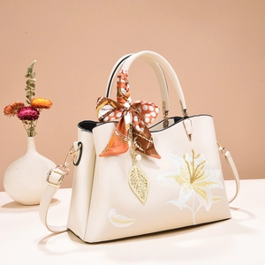 Detailed embroidery of white lilies on beige faux leather handbag with silk scarf handle