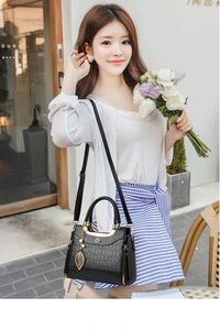 Chic black crocodile pattern handbag with gold leaf charm held by a model in casual attire