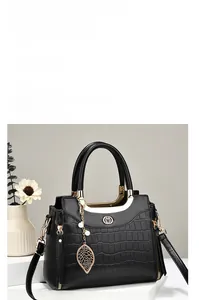 Detail of black crocodile texture handbag with golden leaf pendant and pearl charm