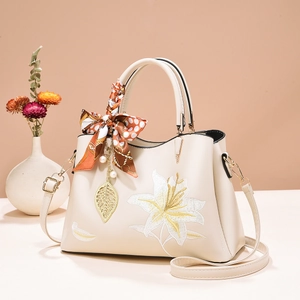 Detail of embroidered floral handbag with silk scarf handle and golden leaf pendant