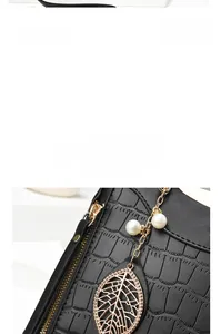 Detail of black crocodile texture leather bag with gold leaf pendant and white pearls