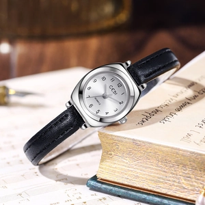 Montre vintage argentée avec bracelet en cuir noir fin sur un livre ancien