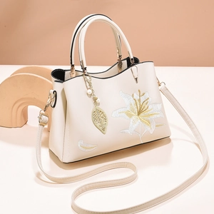 Detail of elegant lily embroidery and pearl leaf charm on beige leather handbag