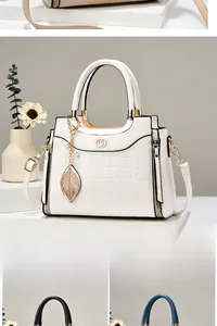 Detail of white crocodile pattern handbag with gold heart logo and leaf charm