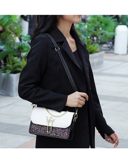 Detail of crossbody bag with sequins and pearl cat pendant on model in black blazer