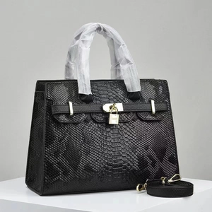 Macro detail of black snakeskin embossed handbag featuring gold hardware and lock