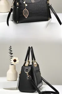Detail view of black crocodile pattern handbag with golden M logo and leaf pendant charm
