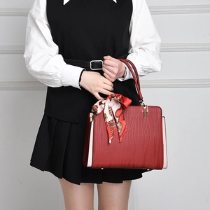 Detail of red textured leather handbag featuring decorative scarf and gold hardware