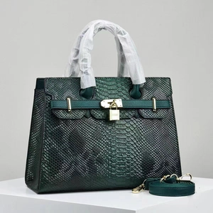 Macro shot of dark green snakeskin embossed leather bag with gold metal lock and strap