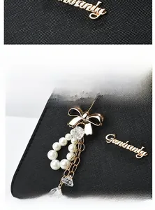 Détail d'un sac à main en cuir noir texturé avec logo doré et breloque nœud en perles