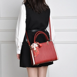 Detail of red leather handbag with wave texture, decorative scarf and metal base studs
