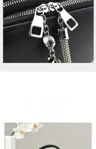 Detail of black lychee leather bag featuring double silver zippers and rhinestone cat tassel