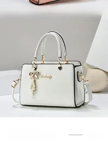Détail d'un sac à bandoulière blanc avec logo doré et breloque en perles élégante