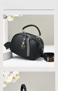 Detail of black pebbled leather handbag featuring silver zippers and patterned wide strap