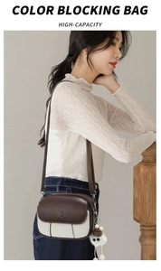 Detail of color-blocking crossbody bag in brown and cream PU with pom-pom charm