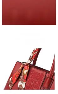 Close-up of red lychee leather handbag with floral embroidery and decorative silk scarf