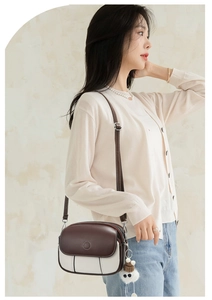 Detailed side view of women's crossbody bag in brown and white with furry pompom charm
