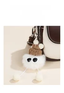Detail of creative white plush charm with mini knit hat and sunglasses on leather handbag