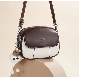 Detail of two-tone crossbody bag with top flap, dual zippers, and cute pom-pom charm