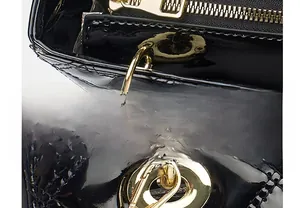 Detail of quilted patent leather texture and smooth gold zipper on black handbag