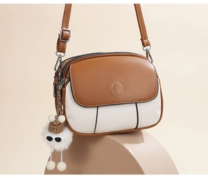 Detail of color-block crossbody bag featuring dual zippers and cute plush charm pendant