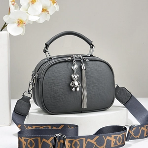Grey textured leather handbag with wide shoulder strap and metal bear charm accessory