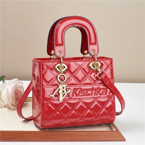 Red quilted patent leather lady bag with gold charms and top handle on wooden tray