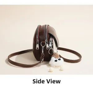 Detail view of brown crossbody bag with triple zippers and cute plush charm accessory