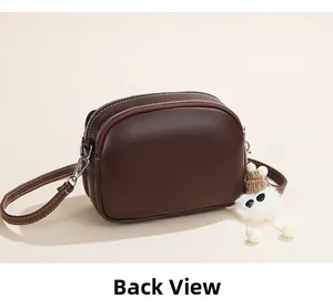Back view of a dark brown double zipper shell bag with a cute plush pompom accessory