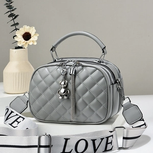 Grey quilted crossbody bag with bear pendant and sporty logo strap on geometric display